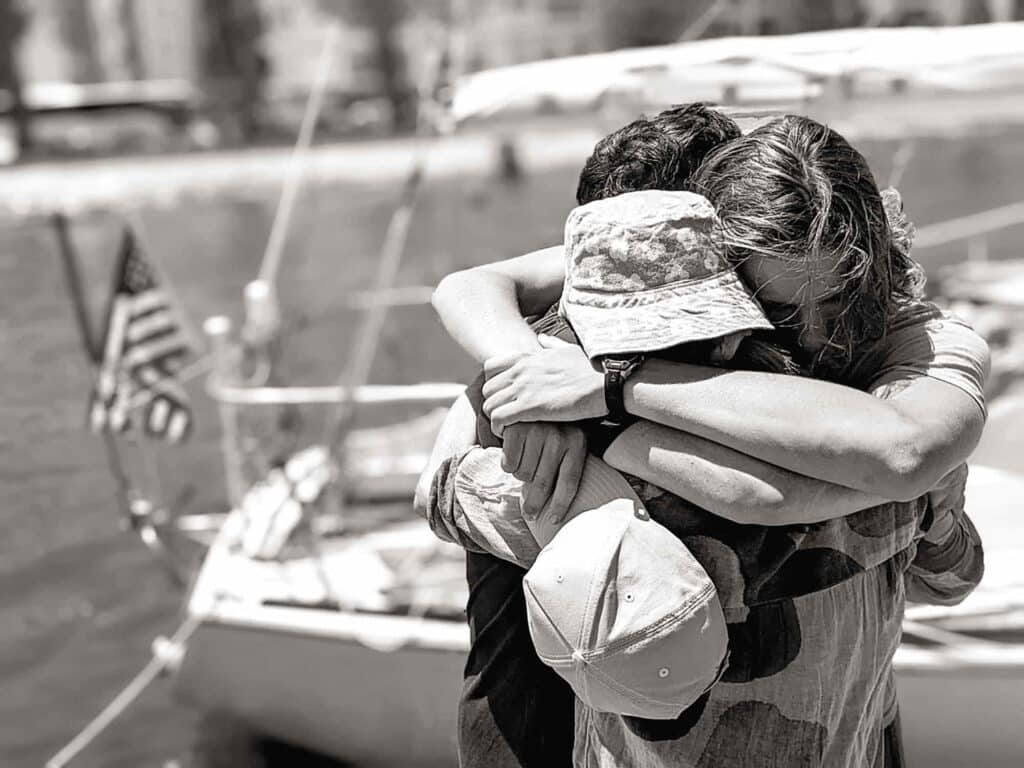 A black and white photo of people hugging on a boat dock.