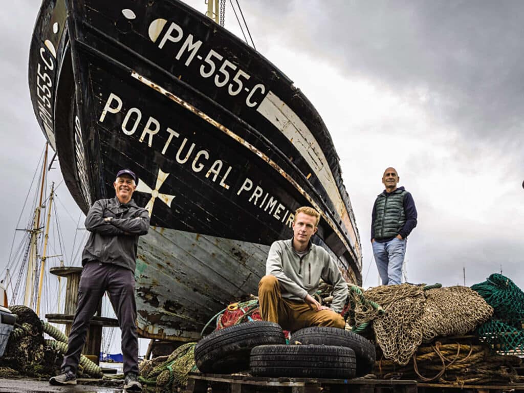 An image of three men standing in front of a boat.