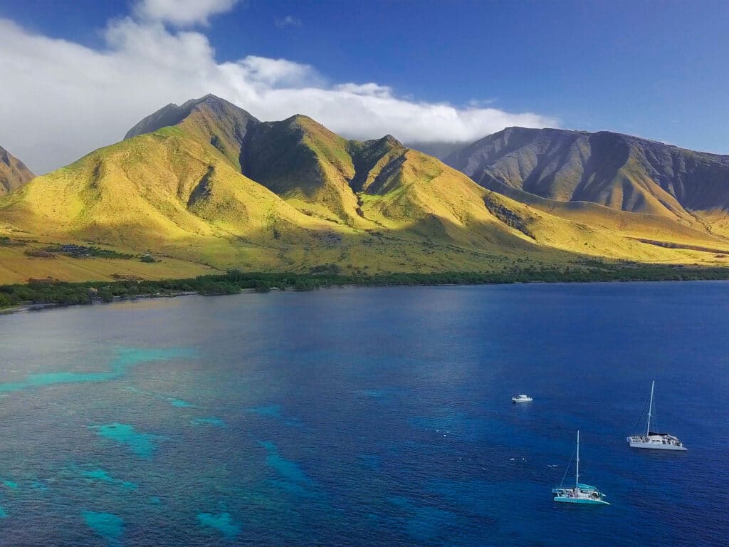 Coast of Maui with visible coral reef, sailing boats and green mountain on the background. Area of Olowalu, Hawaii