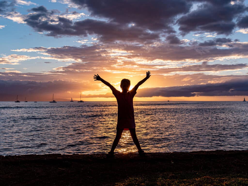 Silhouette of a little girl standing with hands in the air against scenic sunset, Lahaina bay, Maui, Hawaii