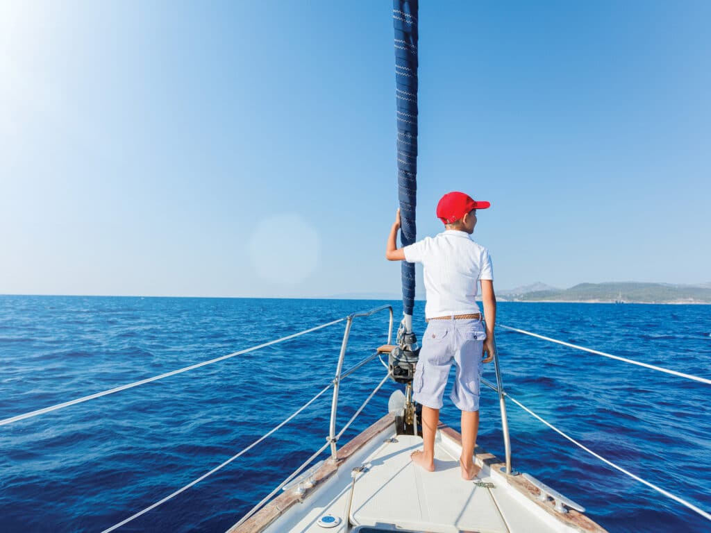 Little boy on board of sailing yacht on summer cruise. Travel adventure, yachting with child on family vacation.