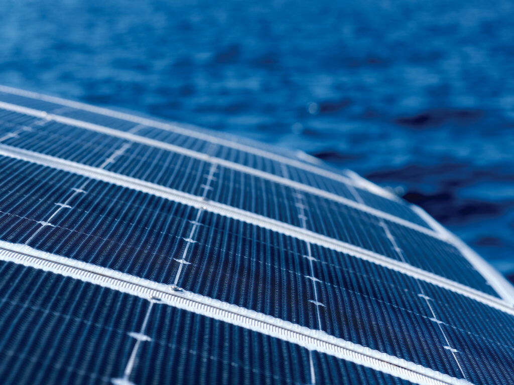 Close up view part of solar panel on dock of sailboat and blue sea waters during sunny day outdoors