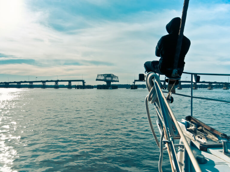 Man sitting at the bow, on a sailboat, relaxing and watching a swing bridge opening to let sailboats through