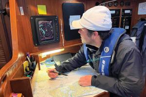 a sailor cross-references a paper chart with radar targets